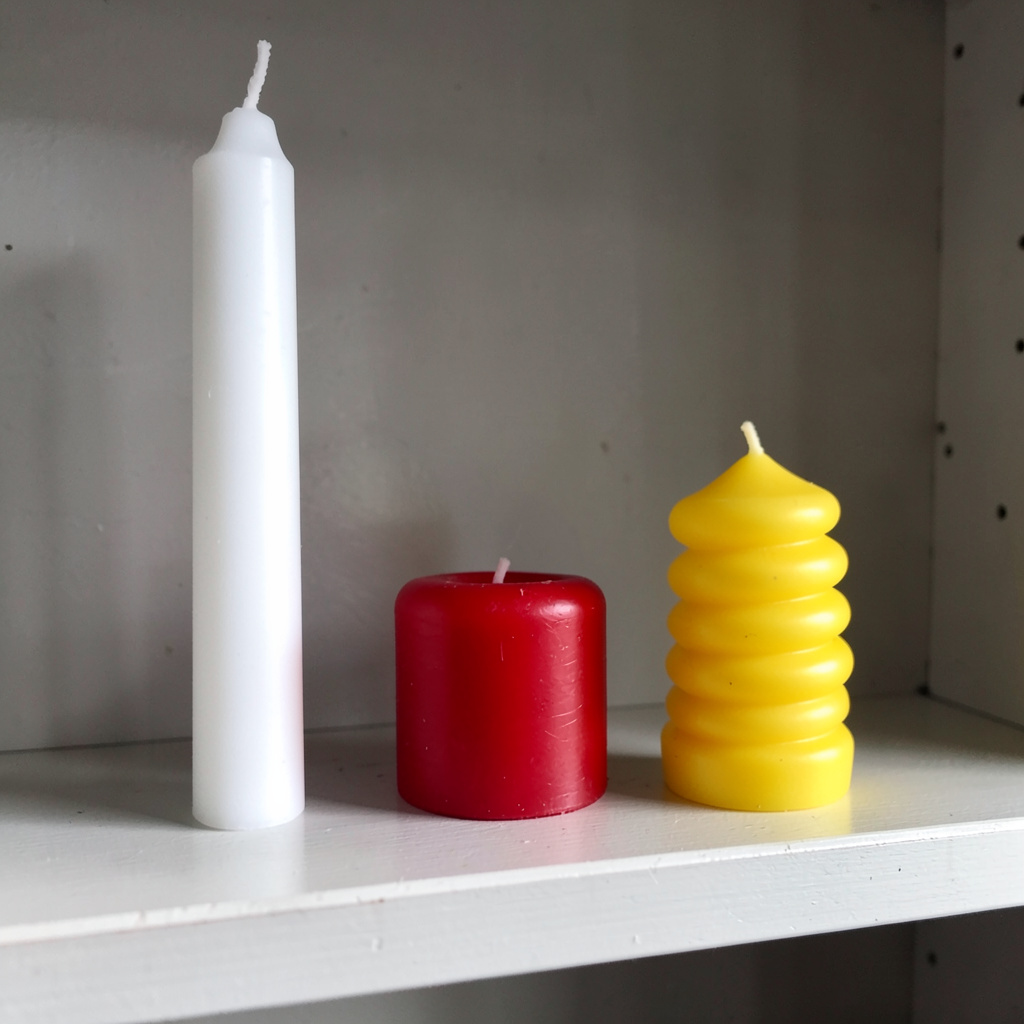 A tall thin white candle, a short fat red candle, and a medi
