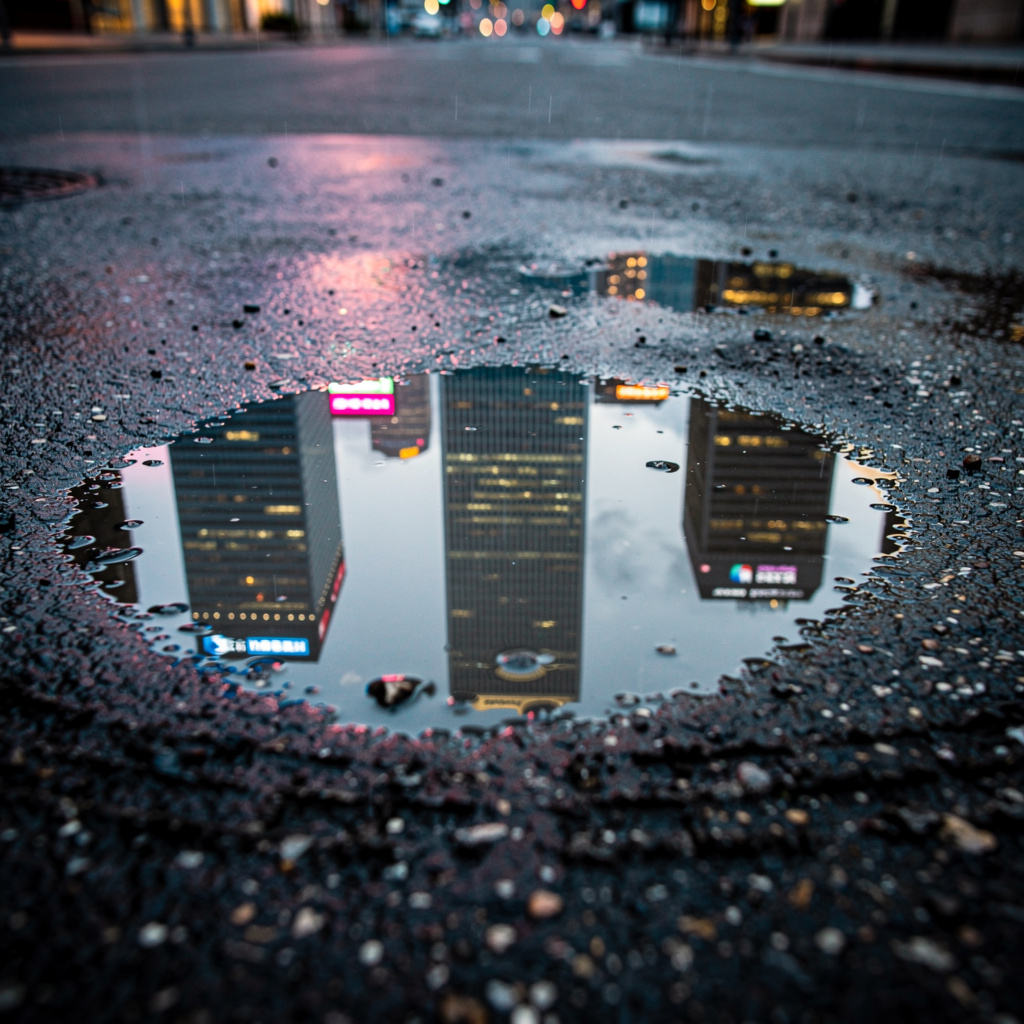 A city skyline reflected in a rain puddle on a street, with 