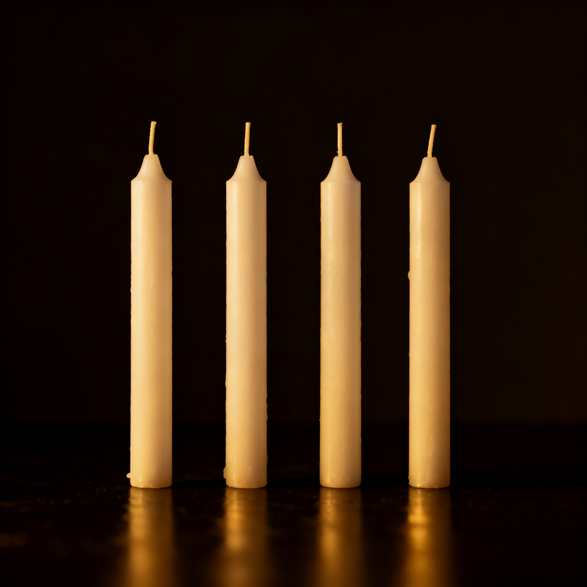 Exactly 4 white candles standing on a dark surface