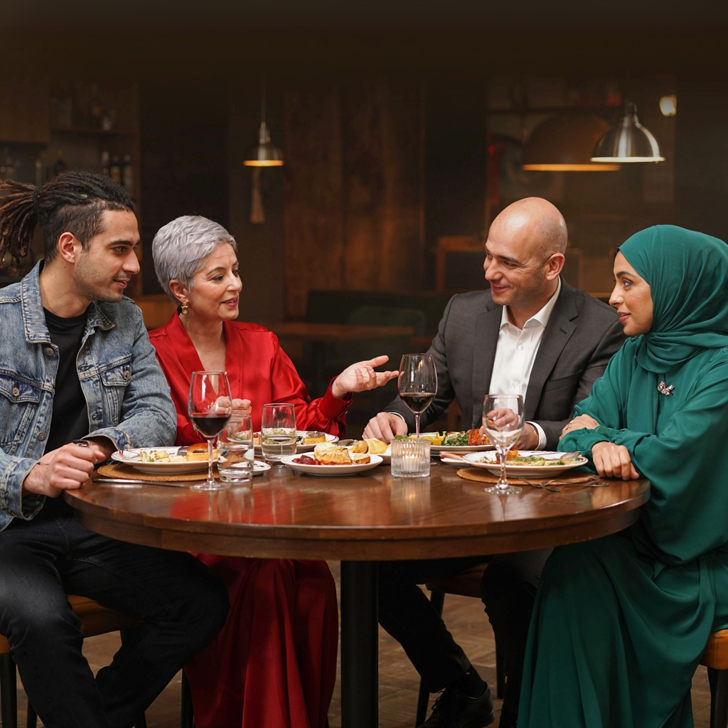 Four people at a dinner table: a bald man in a suit, a woman