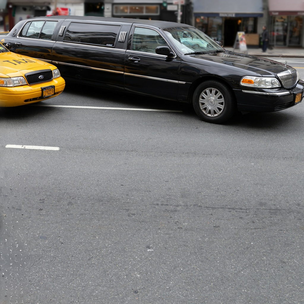 A yellow taxi and a black limousine parked next to each othe