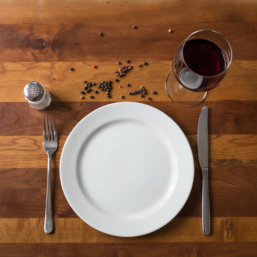 A dinner table scene with a plate, fork, knife, wine glass, 