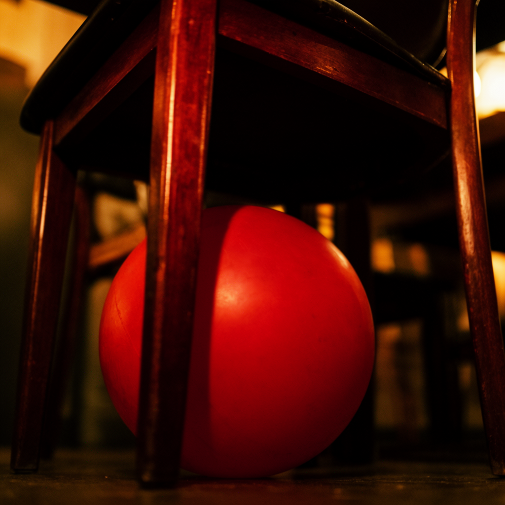 A red ball underneath a wooden chair