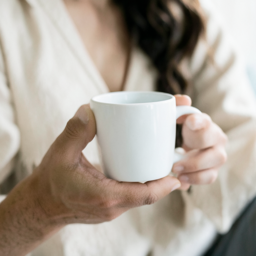 A person holding a white ceramic coffee mug by the handle wi