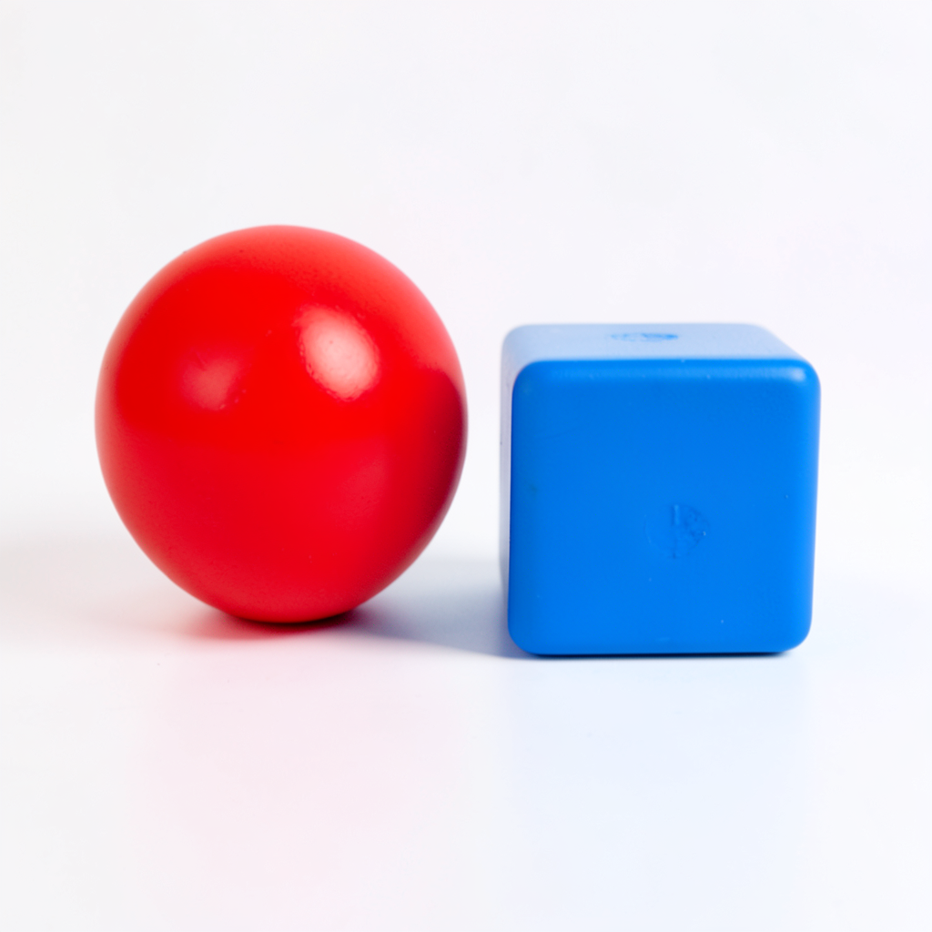 A red ball and a blue cube sitting side by side on a white s