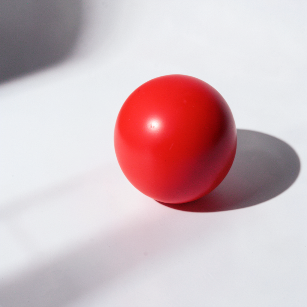 A red sphere on a white surface with a single shadow cast to