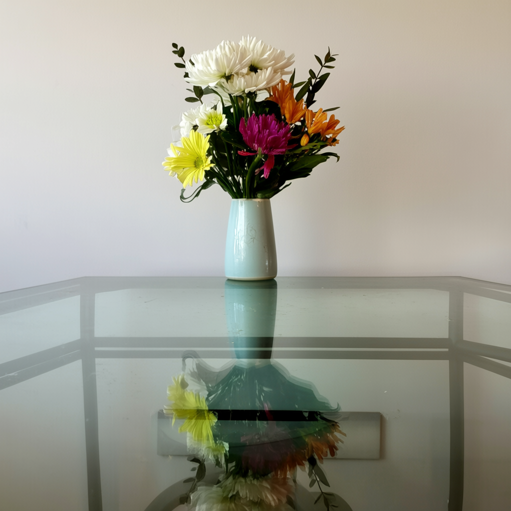 A vase of flowers on a glass table with a clear reflection v
