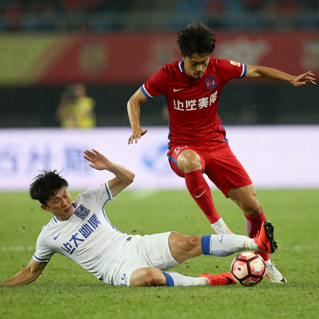Two soccer players mid-tackle, one sliding and the other jum