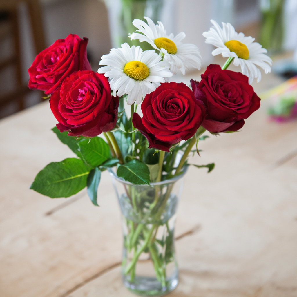 4 red roses and 2 white daisies in a glass vase on a table